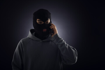 Criminal in mask talking on phone against dark background. Space for text