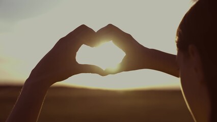 girl shows her heart with hands against background heavenly sunset. close-up. valentine in female...