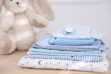 Stack of clean baby clothes and accessories on wooden table indoors, closeup