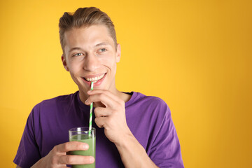 Man drinking juice through straw on orange background, space for text
