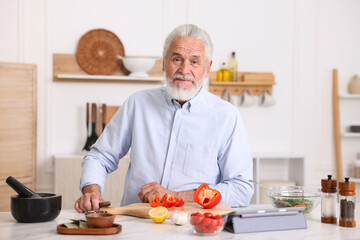 Elderly man cooking at white marble table in kitchen
