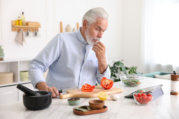Elderly man using tablet while cooking at white marble table in kitchen