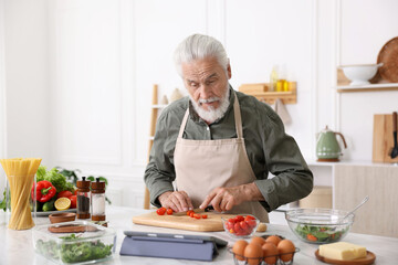 Elderly man cooking at white marble table in kitchen