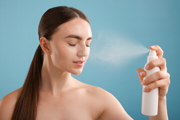 Beautiful woman spraying thermal water onto her face on light blue background