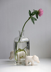 Still life with two toy elephants and a red clover flower in a small glass vase.