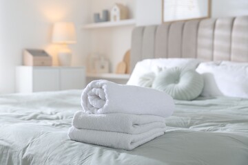 Stack of clean towels on bed linens at home