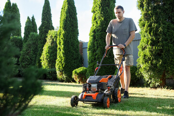 Man cutting green grass with lawn mower in garden