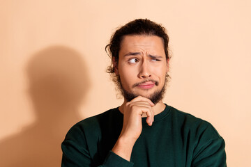 Thoughtful young man in casual fashion posing on beige background with a curious expression and stylish green pullover