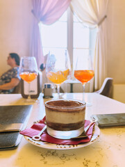 Classic Italian tiramisu dessert with cocoa powder served on a marble table, paired with refreshing Aperol Spritz cocktails in a cozy Venetian café