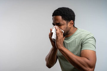 Man blowing nose due to allergy or cold on isolated background, sick adult, seasonal illness concept