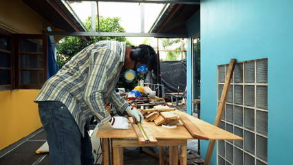 Carpenter measuring wooden plank with tape measure on outdoor workbench wearing gloves and safety...
