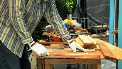 Carpenter aligning wooden planks on workbench while wearing gloves and protective gear for...