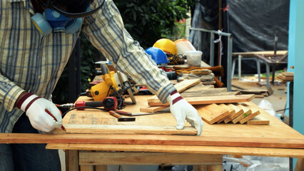 Carpenter in gloves marking measurement with pencil on wooden plank on workbench in workshop