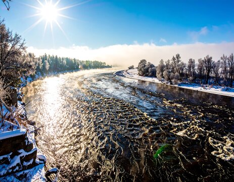 A winter scene of a river with frosty trees and sparkling water, bathed in sunlight. - Powered by Adobe