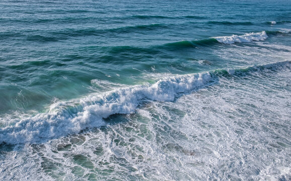 Fototapeta Sea water with foamy surface and waves. Close-up top view of green and blue rushing water near the shore