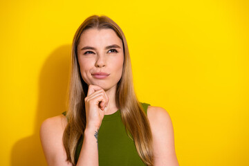 Thoughtful young woman in a green top on a yellow background, contemplating and smiling,...