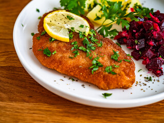 Breaded chicken breast with boiled potatoes and beets on wooden table	