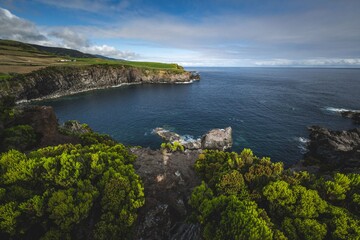 Obraz premium Coastal view with greenery and rocky cliffs meeting the deep blue sea on Terceira island, Azores