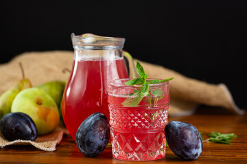 Fruit juice with a colorful shade next to pears and plums © Peredniankina