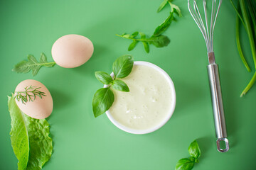 Homemade mayonnaise with herbs and eggs on a green background