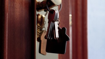 Apartment keys with house shaped keychain swinging on golden door handle closeup - Powered by Adobe