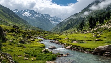 Obraz premium Mountain valley with a clear stream. Lush green meadows and rocky outcrops meet snow-capped peaks under a partly cloudy sky