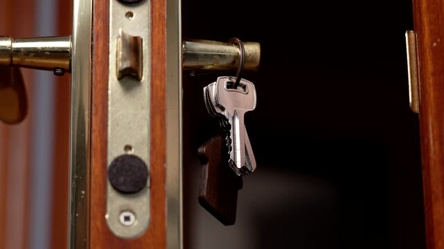 House keys hanging on an old door handle with golden lock. Wooden brown keyring in the shape of building
