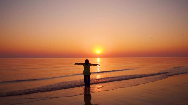 Young woman raising hands on beach during sunset at Mandvi, Gujarat, India. Summer holidays at tropical island. Small waves crashing on shore and sun setting on horizon. Relaxation concept 