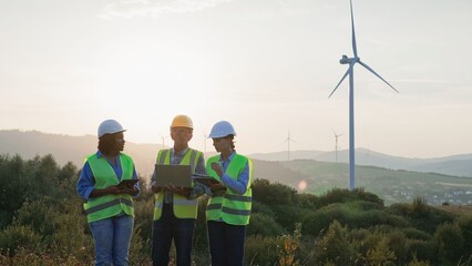 Group of three mixed-raced workers standing in field. Wind energy production concept. People in...