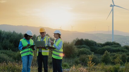 Group of three mixed-raced workers standing in field. Wind energy production concept. People in...