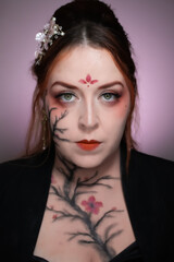 Artistic makeup inspired by sumi-e technique, featuring cherry blossom branches painted across face and neck with elegant red accents