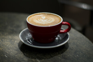 Old fashionedRed Cappuccino cup  with one heart shape on the coffea foam on grey plate.