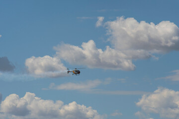 Helicopter flying with smoke trail across dramatic cloudy sky.