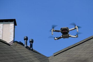 Drone in the air inspecting the roof over the house closeup on blue sky background