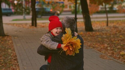 Child girl runs to grandfather, hugs him in autumn park. Carefree childhood, joyful hugs of child...