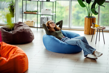 Young woman enjoying relaxation on a bean bag chair in a bright modern interior space, featuring creativity and comfort