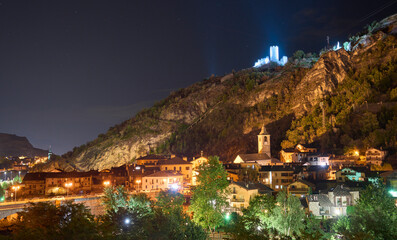 Night view of a town Villeneuve in the Aosta Valley in Italy. The ruins of the medieval castle Chatel-Argent, illuminated by portholes, on the top of the hill above the town. Temple and bell tower.