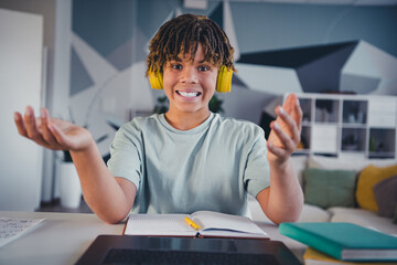 Smiling teenage boy enjoying online learning at home, wearing yellow headphones, seated at a desk...