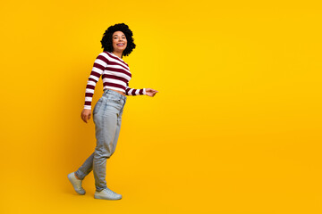 Fototapeta premium Confident young woman in striped top walking confidently against yellow background showcasing casual modern style
