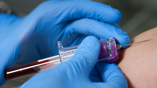 A healthcare professional collects a blood sample from a patient's arm using a syringe in a sterile environment.