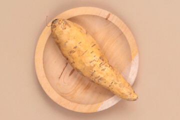 A single Cilembu sweet potato placed on a round wooden plate with a soft beige background,...