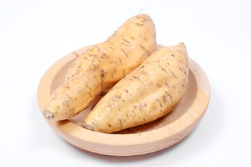 Two fresh Cilembu sweet potatoes placed on a wooden plate with clean white background, showing natural texture and rustic appeal, perfect for concepts of healthy food and organic produce.