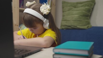 school girl headphones does homework laptop while sitting table room. children classes online home. student concept. girl daughter writes with pen notebook. remote school home learning child. school - Powered by Adobe