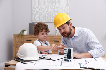 Choice of profession. Father and his son exploring house model at table indoors
