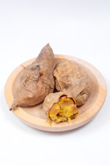 Roasted Cilembu sweet potatoes on wooden plate, showing golden flesh with caramelized texture, delicious organic root vegetable from Indonesia.