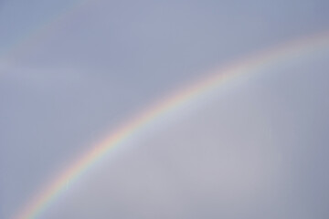 Subtle arc of a faded rainbow across a softly lit sky after light rain.