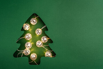 Shiny disco ball string lights glow inside a green Christmas tree paper cutout, blending festive cheer with modern, party-inspired style. Ideal for festive greeting cards, holiday banners