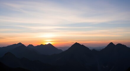 Photo of silhouette of mountain peaks against a colorful sunrise sky with soft clouds