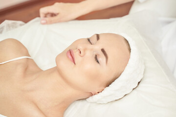 Caucasian young female relaxing during skincare routine in spa setting with headband and closed...