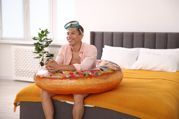 Happy man with diving mask and inflatable ring on bed at home. Dreaming about vacation at sea